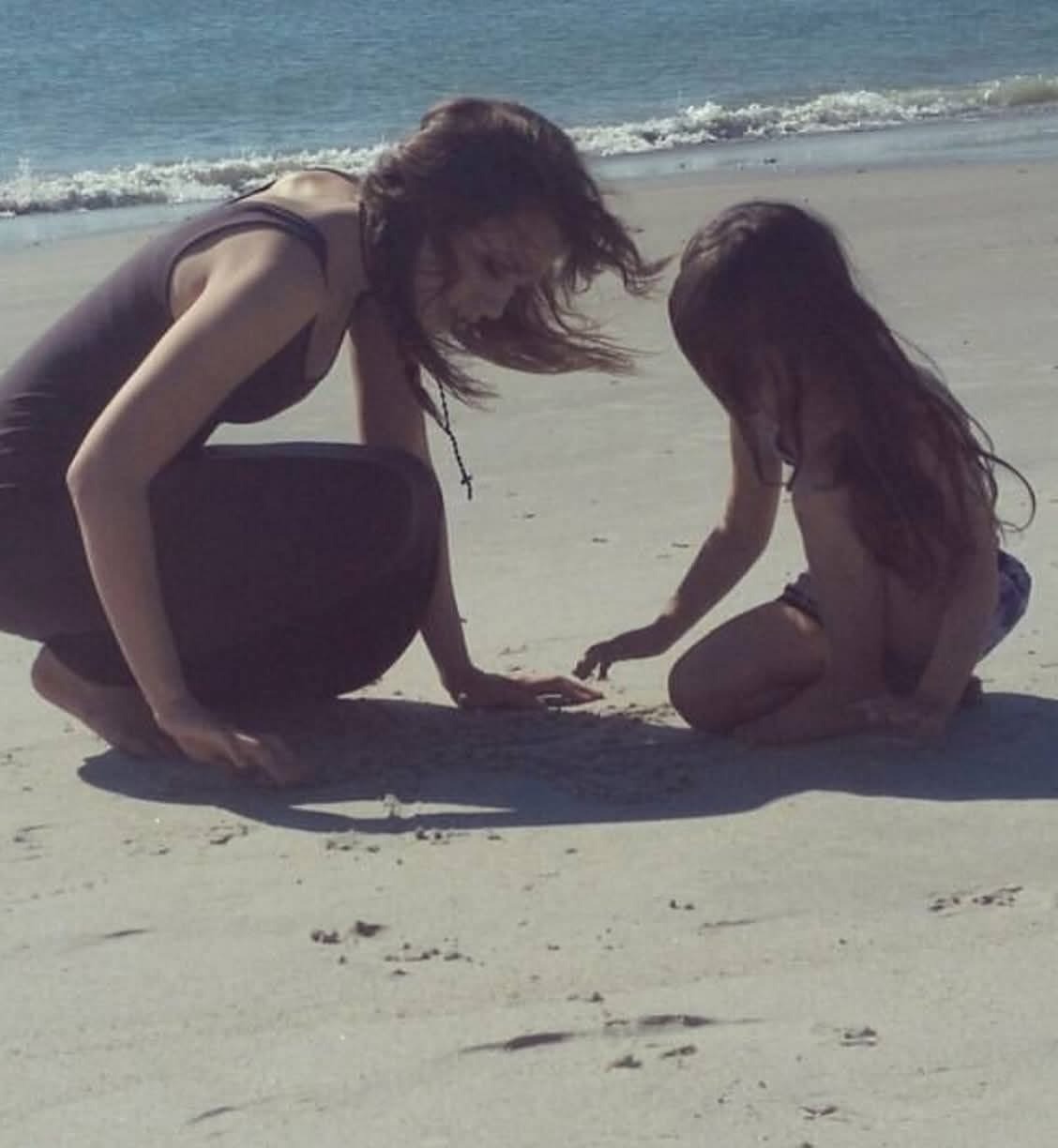 Kneeling in the sand at the ocean's edge with a young girl