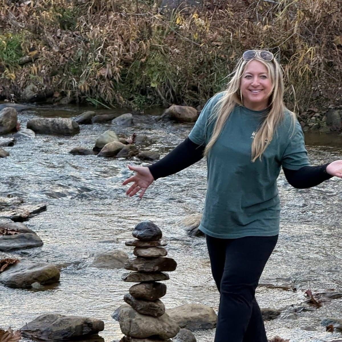 Liz beside a creek with a tower of stacked stones