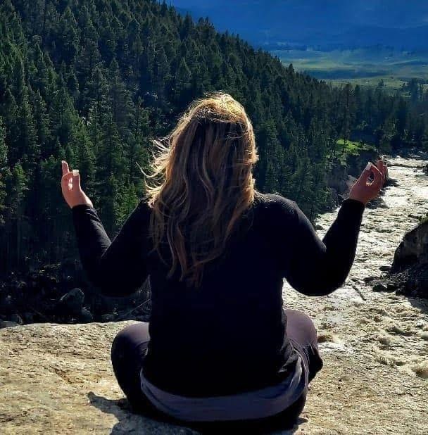 Liz seated in stillness above a rushing mountain river, arms open